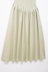 Détail de la jupe trapèze vert clair plissée avec taille asymétrique et texture fluide