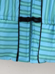 Close-up of traditional black frog fastener on a light blue striped quilted vest fabric