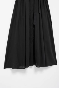 Detailed close-up of black shirt dress featuring vertical pleats and a matching waist tie