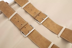 Macro shot of beige fabric with dual caramel faux suede belts and silver metal buckles