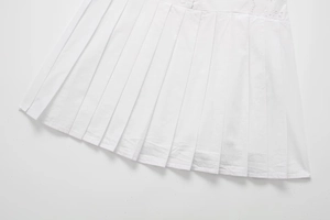 Détail d'une robe plissée blanche élégante avec broderie creuse et lignes de plis nettes