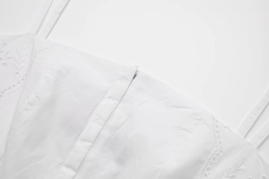 Détail d'une robe d'été blanche avec broderie florale et fines bretelles en coton