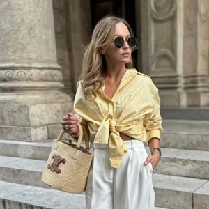 Close-up of a straw bucket bag with a brown leather logo and yellow striped shirt detail