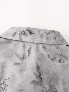 Detailed close-up of light gray beaded embroidery and leaf prints on linen fabric shirt
