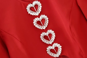 Detail eines roten Kleides mit vier funkelnden herzförmigen Strass-Schnallen