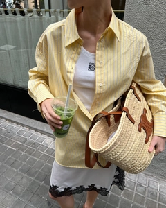 Detail of yellow striped shirt paired with white lace skirt and straw tote bag