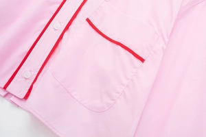 Détail de chemise de pyjama rose avec liseré rouge, poche poitrine et boutons blancs