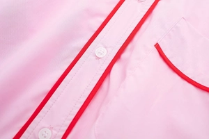 Détail de chemise en popeline rose avec passepoil rouge et boutons blancs aux coutures précises