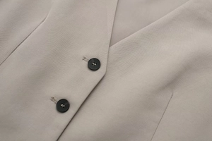 Close-up of black buttons on beige slim-fit vest with refined woven fabric texture