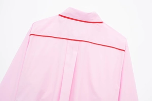 Détail de la chemise rose à manches longues avec passepoil rouge sur le col et coutures