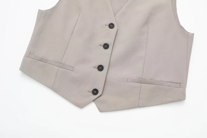 Close-up of light grey V-neck vest showing buttons and pockets on woven fabric