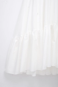 Detailed macro view of white poplin tiered dress featuring ruffled hem layers and smooth texture