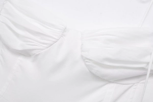 Detailed macro view of white poplin dress featuring pleated bust design and fine stitching