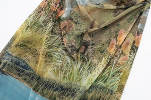 Detail of sheer mesh dress showing green grass and orange floral print with soft pleats
