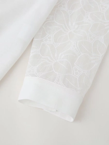Detailed macro view of white floral embroidery on sheer mesh sleeves of a linen blouse