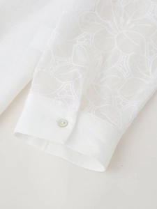 Close-up of intricate floral embroidery on white linen shirt sleeve with pearl button detail