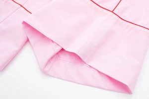 Détail macro du tissu popeline rose avec passepoil rouge et coutures fines au poignet
