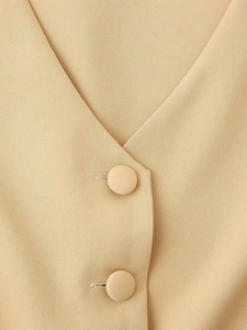 Detail of light beige vest featuring fabric texture and elegant fabric-covered buttons