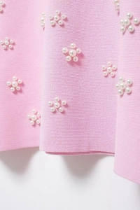 Détail du tissu en maille rose avec décorations de fleurs en perles blanches et texture