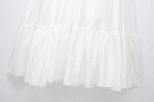 Detail view of tiered ruffled hem on white poplin dress with elegant pleated layering