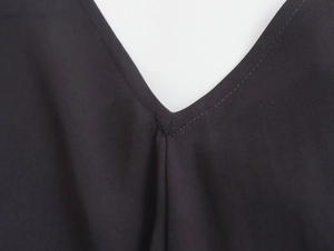 Close-up of V-neckline stitching detail on black sleeveless midi dress with fine fabric texture