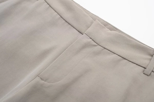 Detailed close-up of light beige trousers showing waistband loops and neat stitching