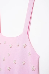 Détail d'un caraco en tricot rose avec fleur de perles blanches et texture douce