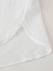 Detailed close-up of white linen shirt showing curved hem with side slit and fine stitching