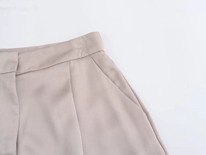 Dettaglio dei pantaloni in raso albicocca a vita alta con tasche laterali e tessuto liscio