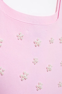 Détail d'une robe en tricot rose avec motifs floraux en perles et texture délicate