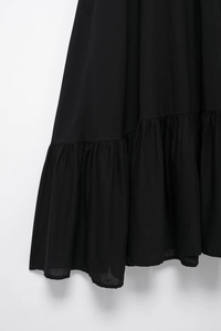 Detail view of layered ruffle hem on a black poplin dress with textured fabric