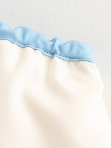 Macro detail showing light blue ruffle trim and cream fabric with precise stitching