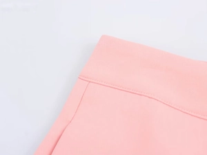 Dettaglio dei pantaloni rosa a vita alta con doppie cuciture e trama del tessuto liscia