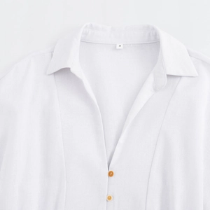 Dettaglio macro di un colletto di camicia bianca in lino con due bottoni marroni e tag S