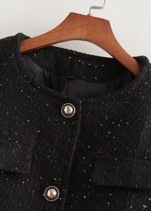 Détail de veste en tweed noir avec paillettes argentées et boutons métalliques gravés