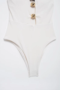 Dettaglio del costume intero bianco con fibbie metalliche dorate e aperture sul davanti