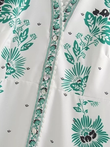 Detail of V-neckline with pearl buttons and green floral print on white summer dress