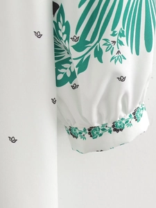 Close-up of elegant green leaf print fabric and decorative cuffs on a white maxi dress
