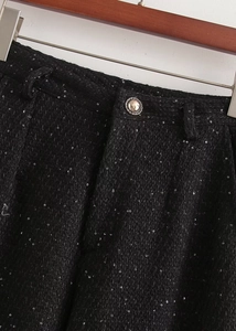 Gros plan sur tissu en tweed noir avec paillettes argentées et bouton en métal vintage