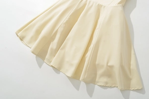 Detail of light beige pleated dress hem with smooth flowing fabric and A-line cut