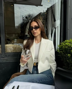 Street style detail of a white cropped blazer paired with a gold buckle leather belt