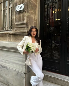 Detail of white cropped blazer with padded shoulders and high-waisted flared pants