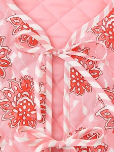 Detalle de chaleco acolchado rosa con estampado floral vintage y lazo de cinta a rayas