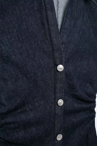 Détail d'une robe en jean bleu foncé montrant des pressions en métal et des plis latéraux