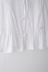 Détail d'un top court blanc avec broderie anglaise, nœuds à nouer et ourlet à volants