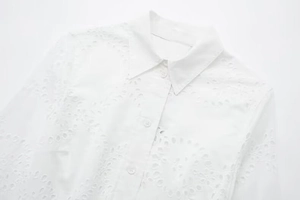 Close-up of white cotton midi dress with intricate eyelet embroidery and buttons