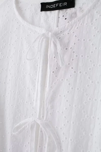 Vue détaillée du chemisier blanc à broderie anglaise avec col lacé et détail d'étiquette