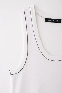 Close-up detail of white knit tank top featuring black contrast stitching and brand neck label
