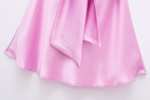 Dettaglio dell'abito in raso rosa con trama lucida e design con fiocco sull'orlo