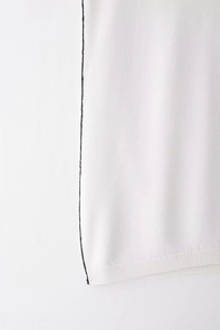 Detailed close-up of white knitted vest with black trim and ribbed hemline finish